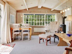 A cozy cabin interior with a dining area, a fireplace, and a large window offering a view of greenery. - 6 Person Holiday Home in Oksbol (Oksbol)