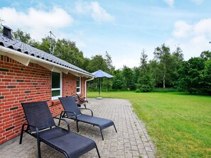 A brick building with a covered patio area featuring two lounge chairs and a table.