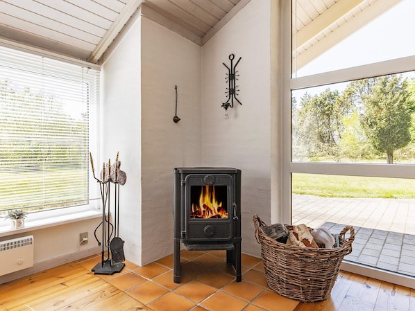 A cozy room with a wood-burning stove, a window with blinds, and a basket of firewood.