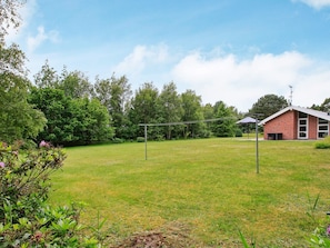 A grassy outdoor area with a brick building, a metal structure, and trees in the background.