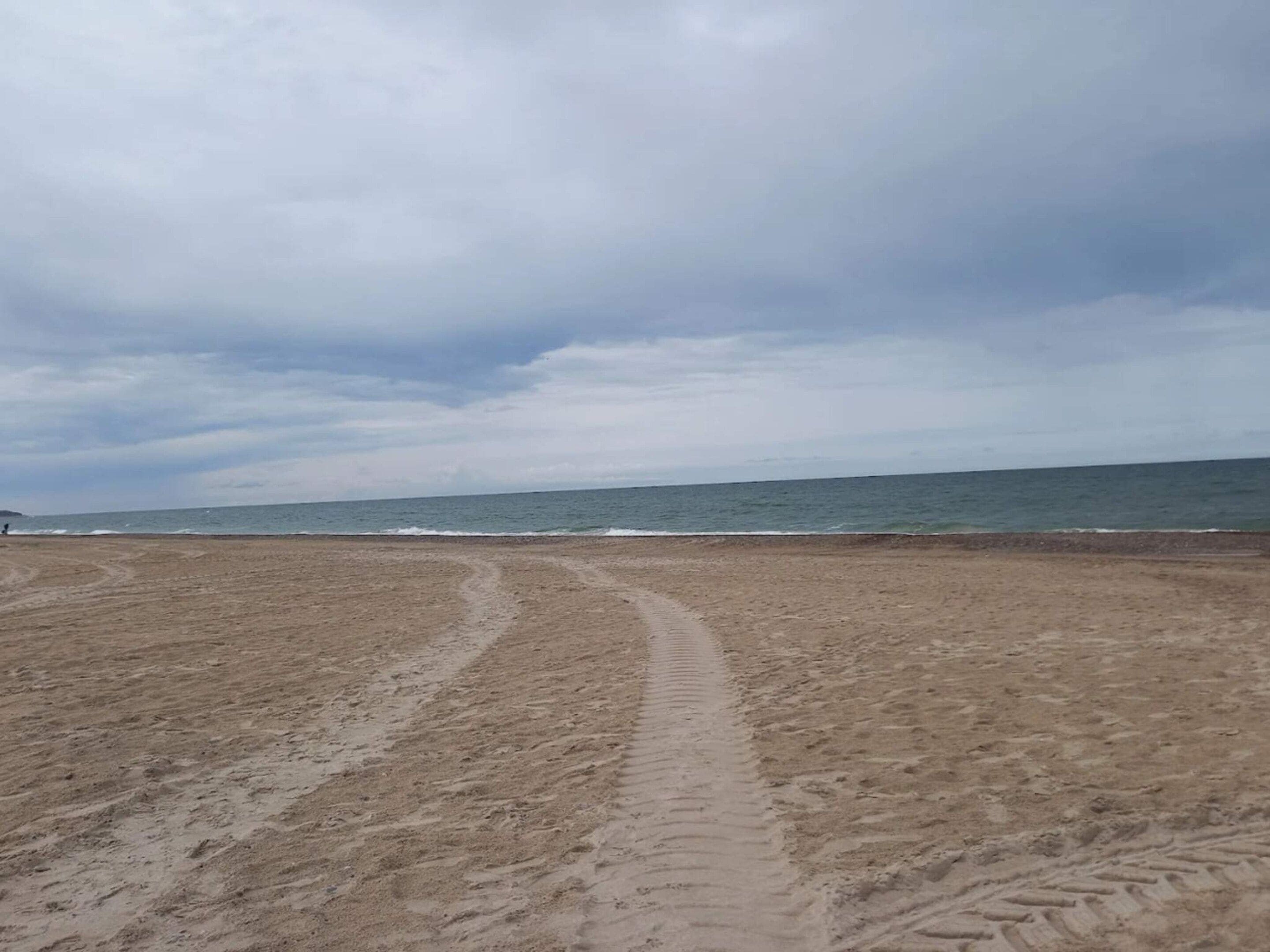 Een zandstrand met een zichtbare route naar het water.