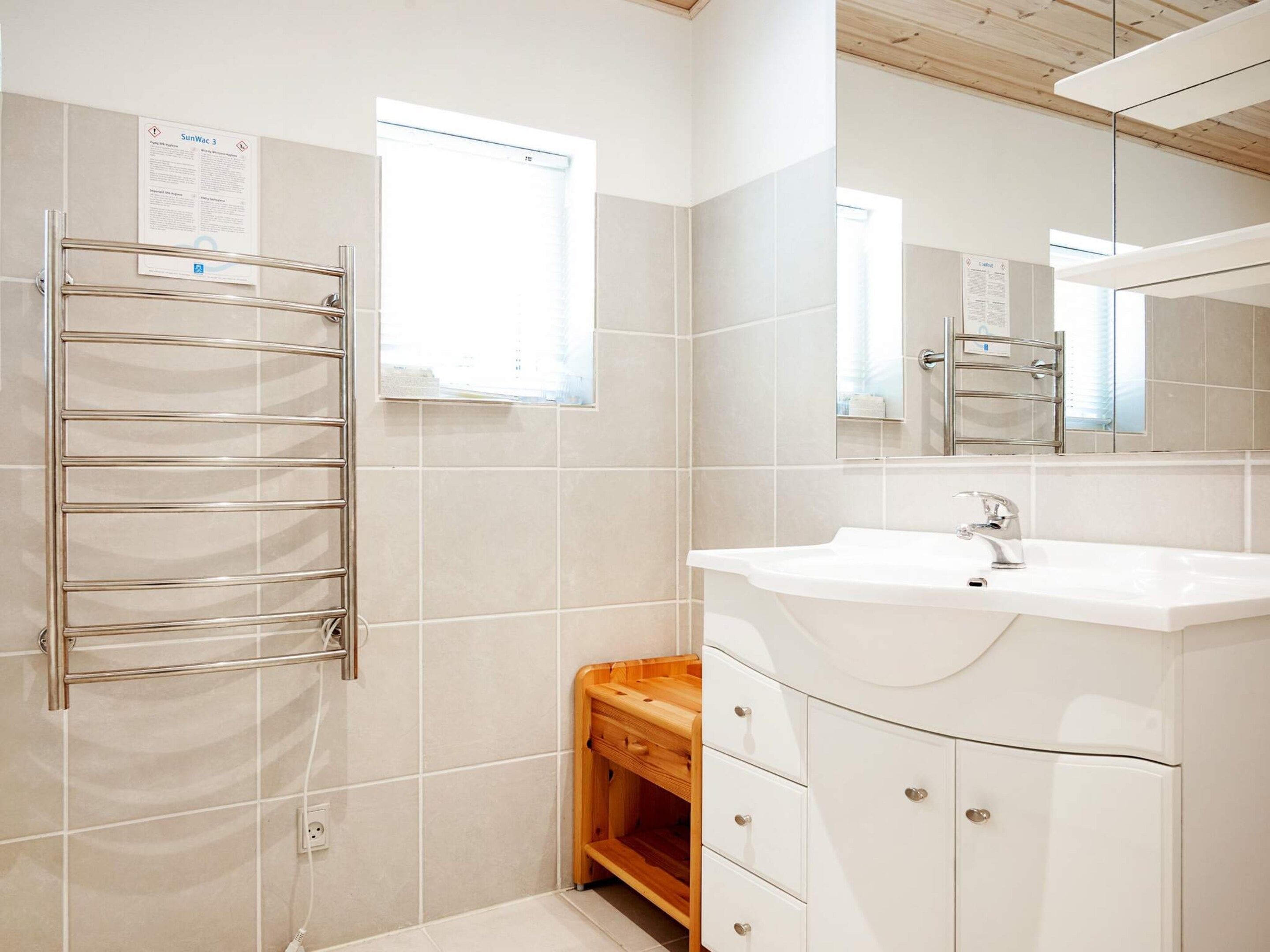 A bathroom with a white sink, a mirror, a towel rack, and a window.