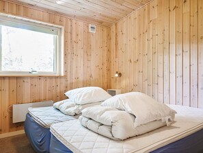 A room with wooden walls, a bed with white bedding, a window, and a radiator. - 4 Star Holiday Home in Thyholm (Thyholm)