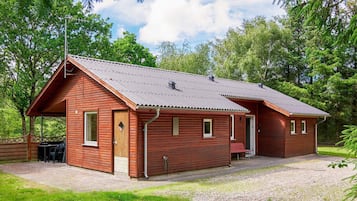 Una baita di legno a due piani con tetto in metallo, un portico coperto e un vialetto sterrato.