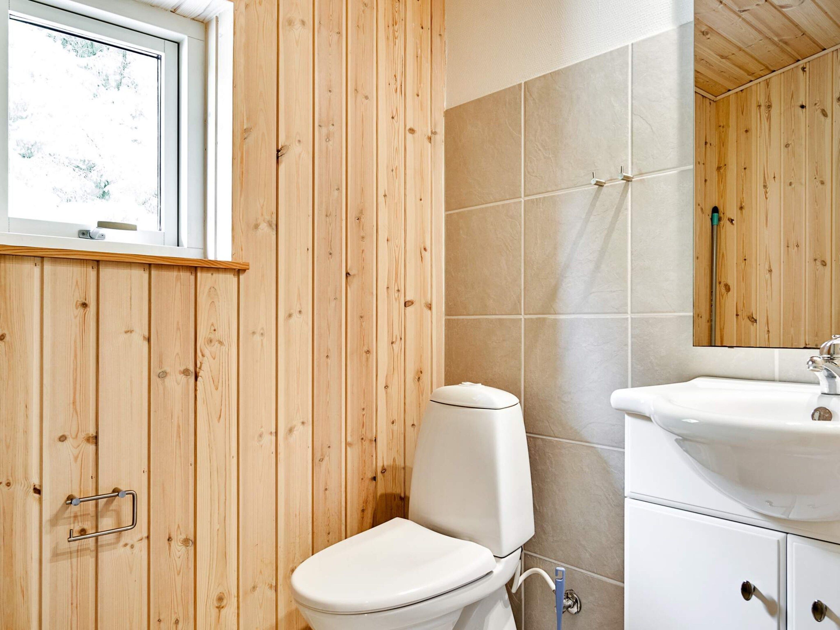A bathroom with a wooden panel wall, a white toilet, a sink with a mirror, and a window.