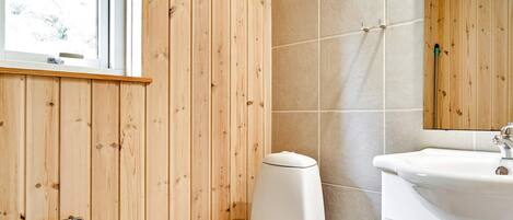 A bathroom with a wooden panel wall, a white toilet, a sink with a mirror, and a window.