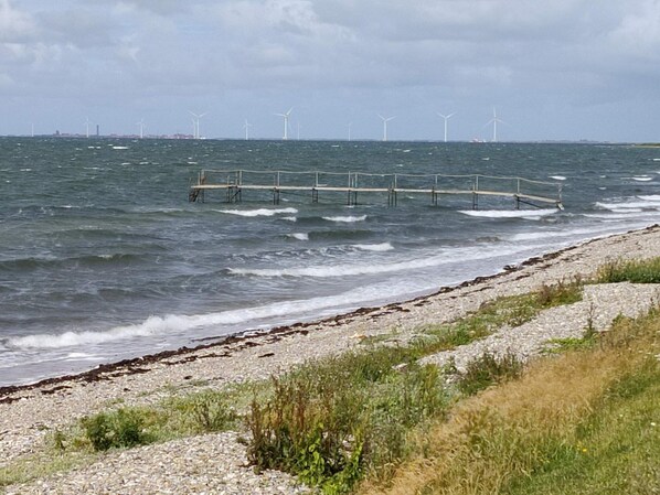 A coastal scene with a rocky beach, waves, and wind turbines in the distance.