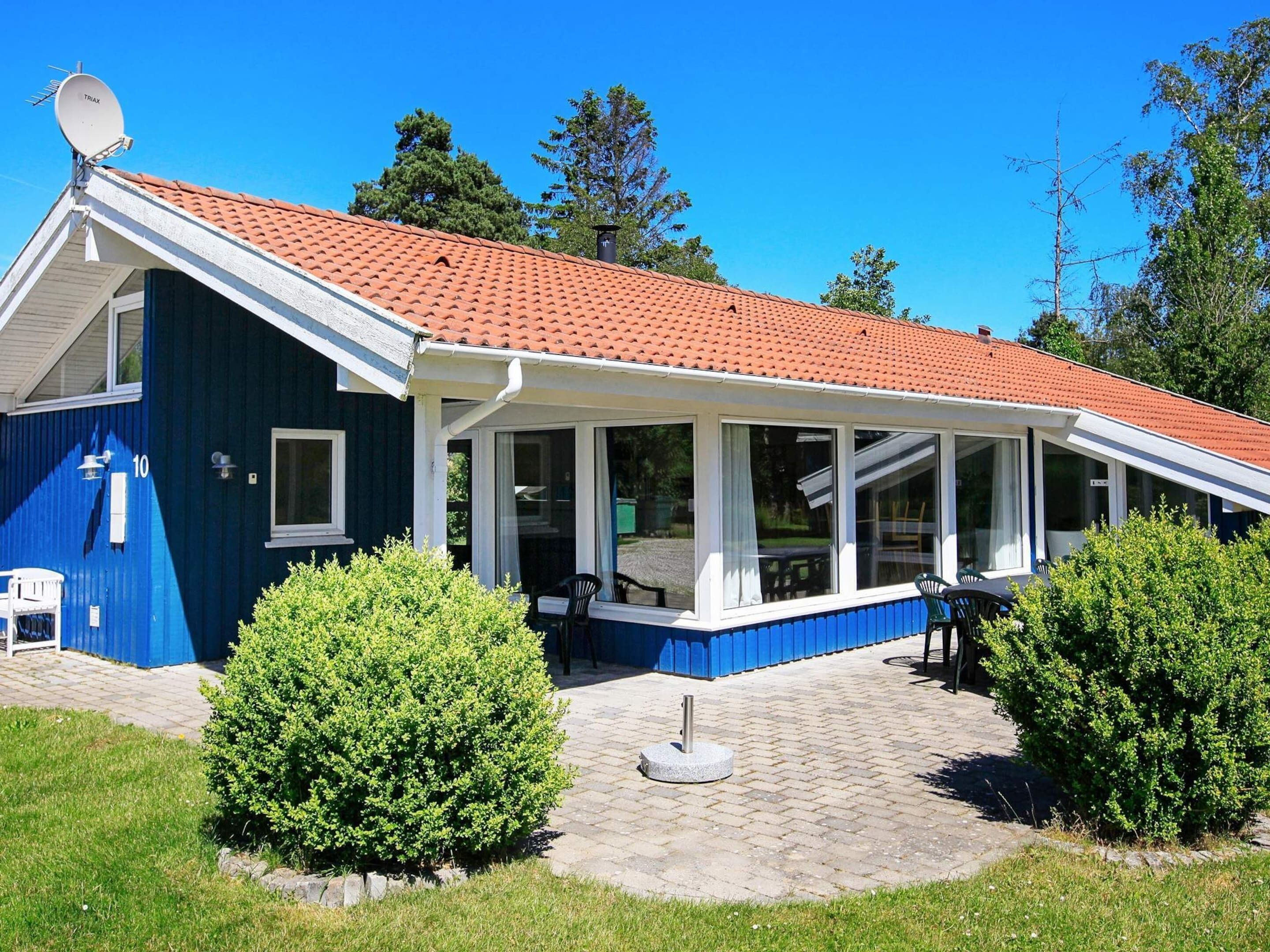 A two-story house with a red-tiled roof, a covered patio with chairs, and a satellite dish.