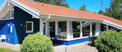 A two-story house with a red-tiled roof, a covered patio with chairs, and a satellite dish.