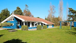 Un bâtiment bleu et blanc avec un toit recouvert de tuiles rouges, une véranda et une balançoire installée dans un espace verdoyant.