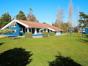 A blue and white building with a red-tiled roof, a covered porch, and a swing set in a grassy area.
