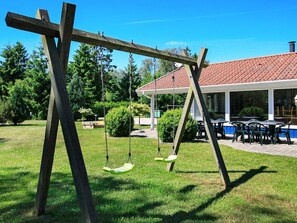 A wooden swing set in a grassy area with a covered patio and outdoor seating in the background.