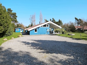 A blue building with a sloped roof, a gravel driveway, and a clear sky.