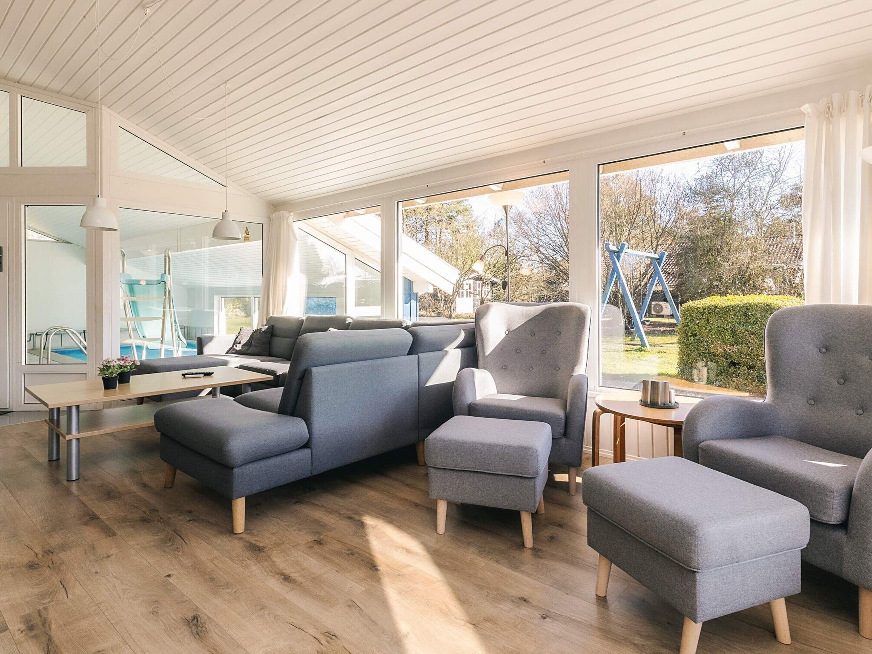 A modern living room with grey upholstered furniture, large windows, and a wooden floor.