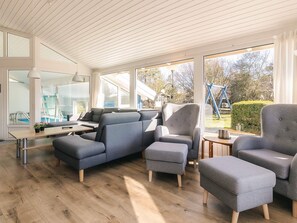 A modern living room with grey upholstered furniture, a wooden floor, and large windows offering a view of the outdoors. - 4 Star Holiday Home in Vaeggerlose (Vaeggerlose)
