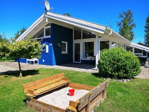A blue building with a sloped roof, a covered patio area, and a wooden sandbox with a red bucket.