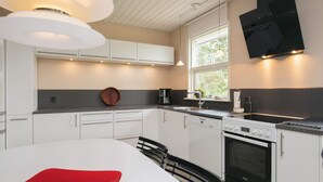 A modern kitchen with white cabinets, a black countertop, a red cutting board, a built-in oven, and a window with a view of greenery outside. - 8 Person Holiday Home in Hjorring (Hjørring)
