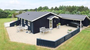 Een gebouw met twee verdiepingen, een overdekte patio, een autoportaal en een schommelset.
