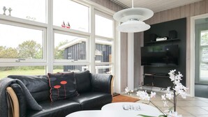 A modern living room with a black leather sofa, a white coffee table, and a red orchid plant. - 8 Person Holiday Home in Hjorring (Hjørring)