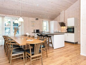 A modern kitchen with wooden cabinets, a central island, and a dining area with wooden chairs and a table. - 5 Star Holiday Home in Romo (Rømø)