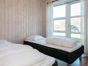 A room with two beds, a window with a view of the outside, and a wooden wall.