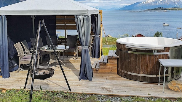A wooden deck with a covered seating area, a hot tub, and a view of a lake and mountains. - 10 Person Holiday Home in Lyngseidet (Lyngen)