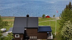 A house with a dark roof, a red building in the background, and a flagpole with a flag. - 10 Person Holiday Home in Lyngseidet (Lyngen)