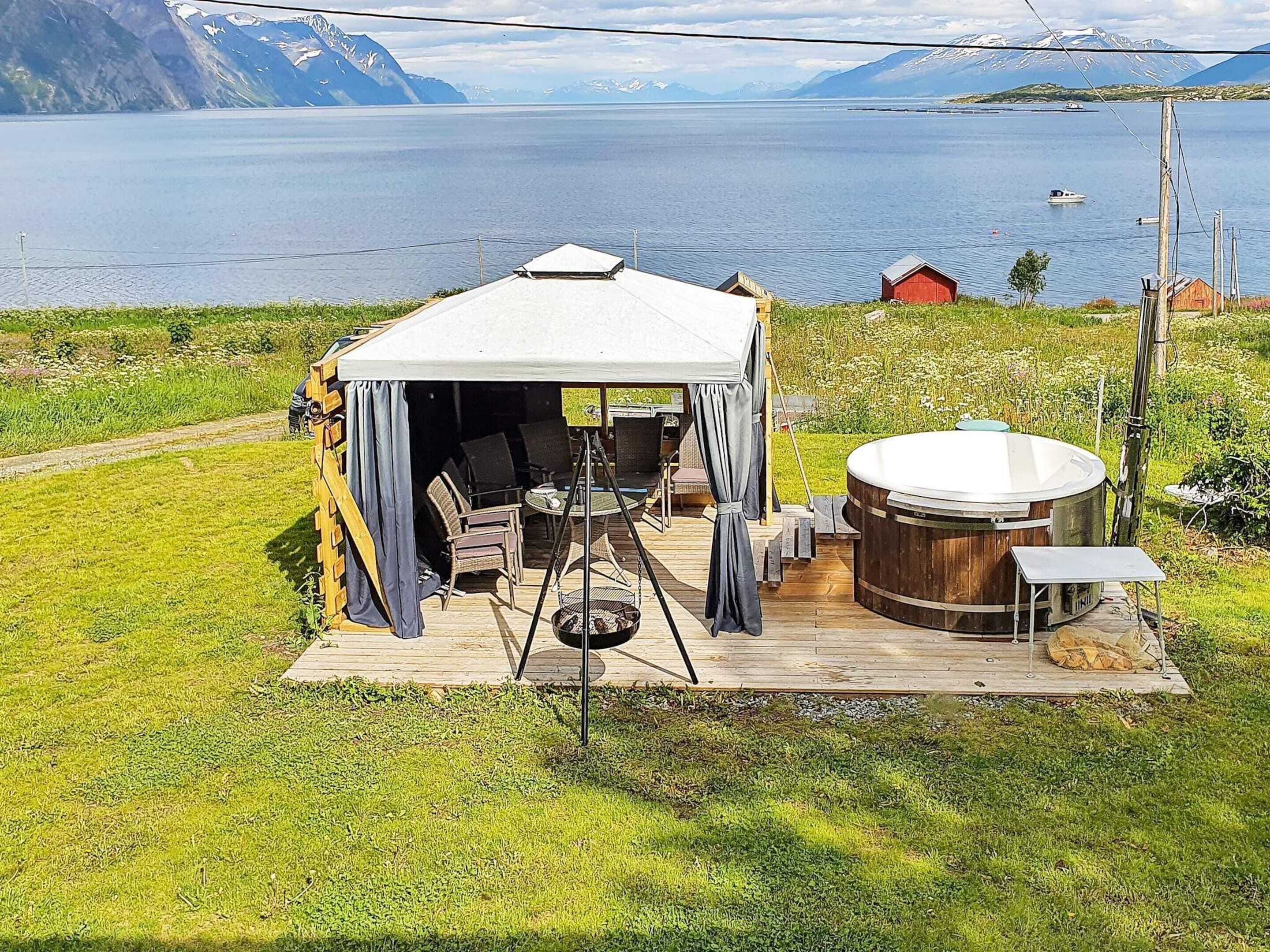 A tent with a table and chairs, a hot tub, and a view of a lake and mountains.