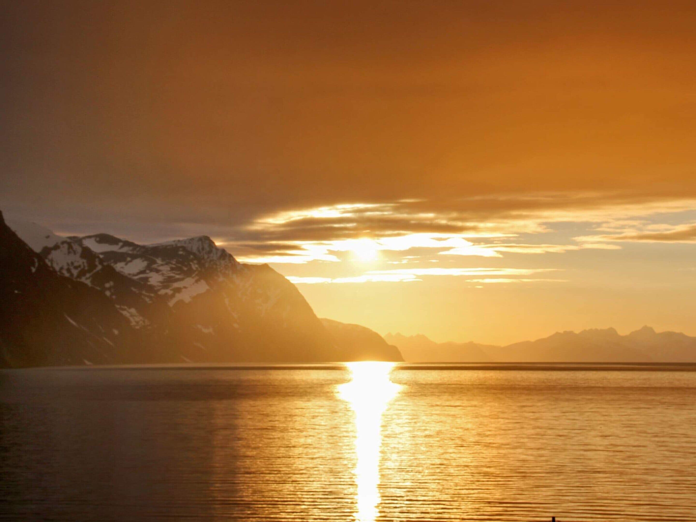 A mountain landscape with a sunset over a calm body of water.