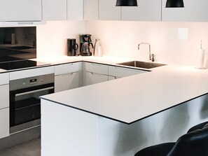 A modern kitchen with white cabinetry, a stainless steel sink, and a built-in oven. - 5 Star Holiday Home in Ringkobing (Ringkobing)