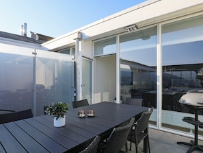 A modern outdoor dining area with a black table and wicker chairs, a potted plant, and a sliding glass door leading to an indoor space.