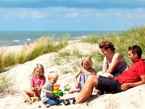 A family of five on a sandy beach with a clear sky and ocean in the background. - 8 Person Holiday Home in Ringkobing (Ringkobing)