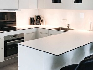 A modern kitchen with white cabinetry, a stainless steel oven, a built-in dishwasher, and a black countertop. - 8 Person Holiday Home in Ringkobing (Ringkobing)