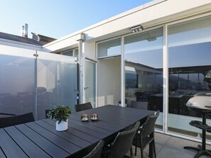 A modern outdoor dining area with a black table and wicker chairs, a potted plant, and a sliding glass door leading to an indoor space. - 5 Star Holiday Home in Ringkobing (Ringkobing)