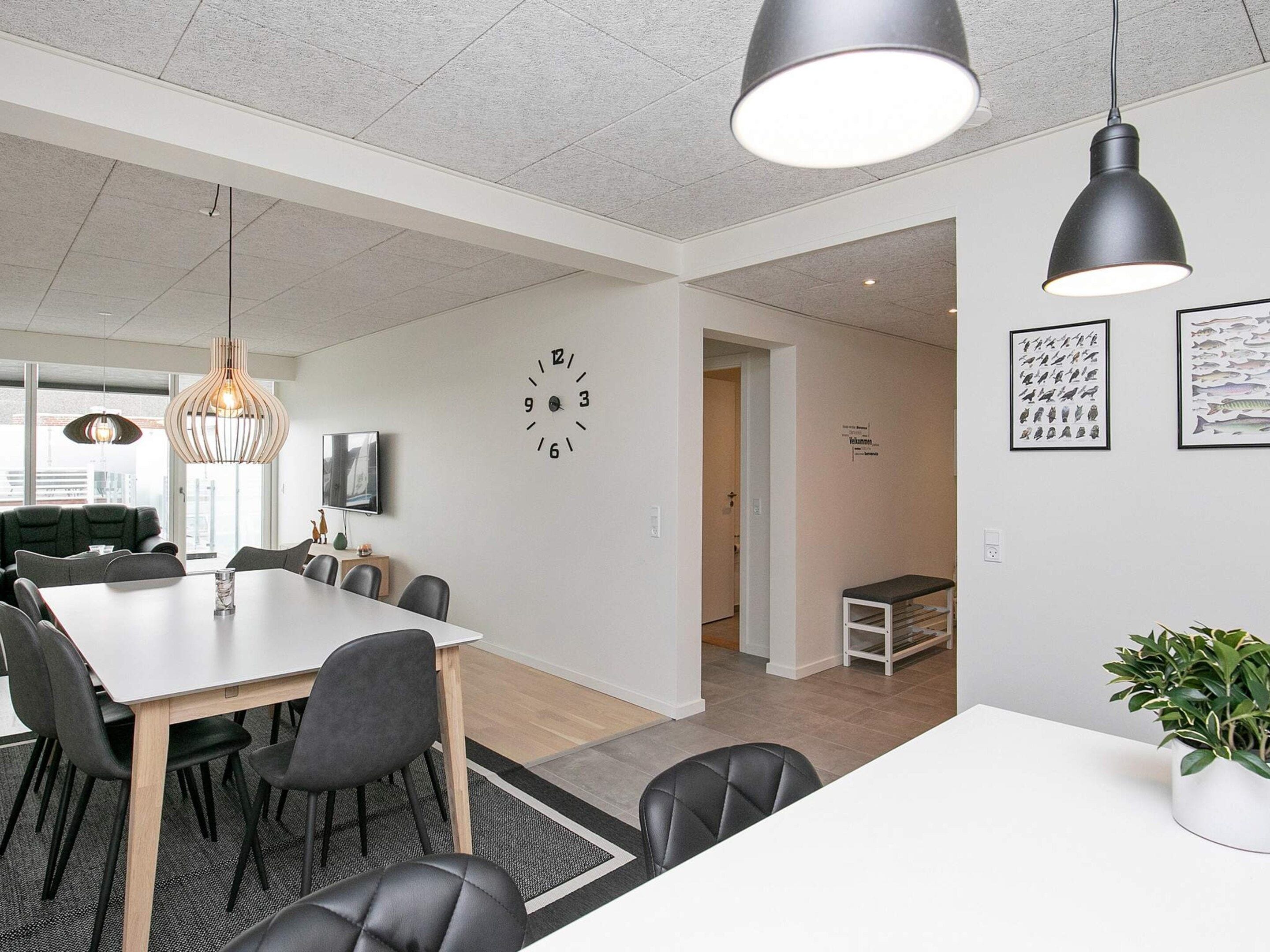 A modern interior with a dining area, a clock on the wall, and a potted plant.