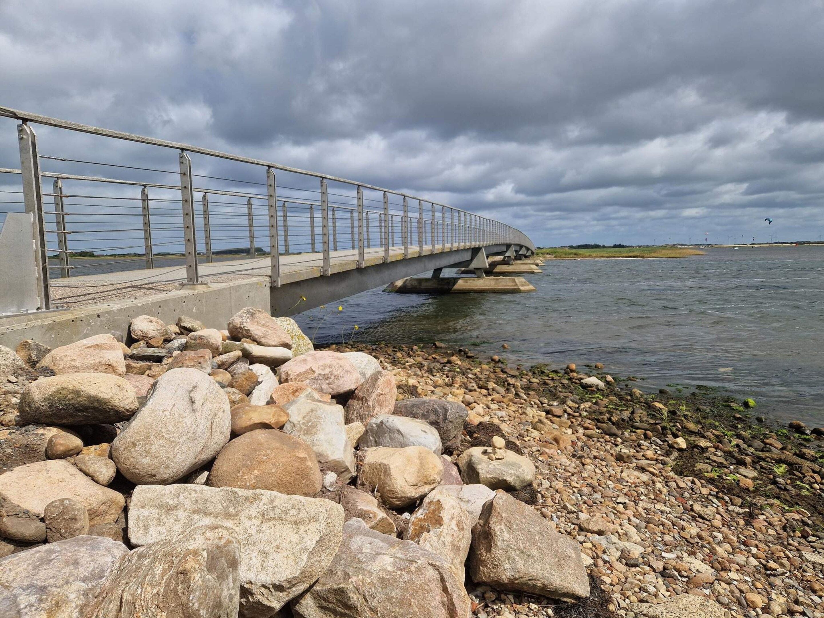 Eine Betonbrücke mit Metallgeländern über einem Gewässer, umgeben von einer felsigen Küste.