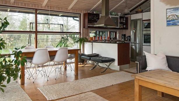 Uma cozinha moderna com uma ilha central, uma sala de jantar com mesa e cadeiras, e uma sala de estar com sofá e mesa de centro.