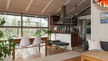 Uma cozinha moderna com uma ilha central, uma sala de jantar com mesa e cadeiras, e uma sala de estar com sofá e mesa de centro.