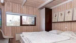 Quarto com cama, poltrona, janela e impressões botânicas emolduradas na parede.