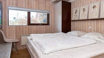 Quarto com cama, poltrona, janela e impressões botânicas emolduradas na parede.