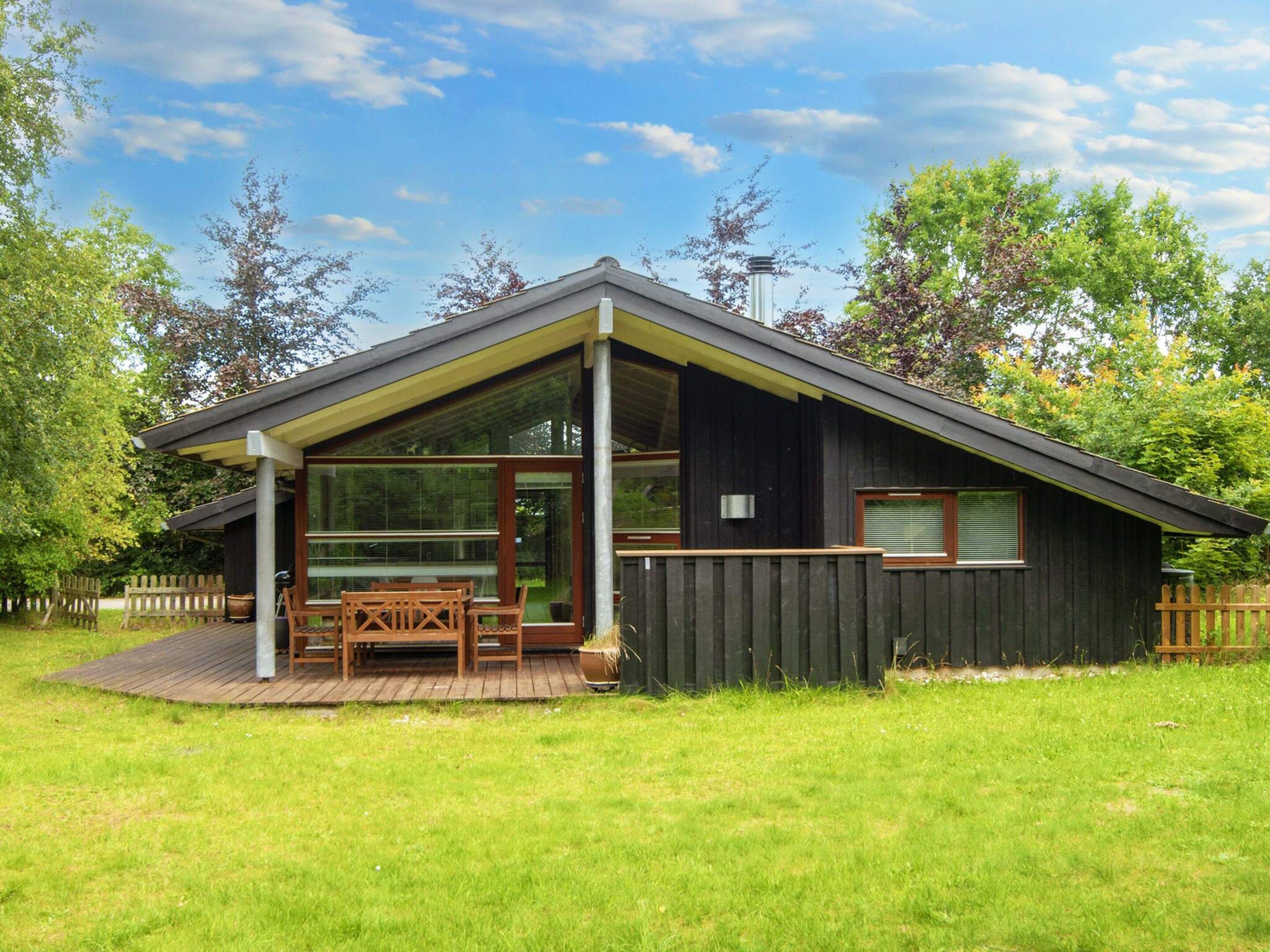 Una casa moderna con un amplio ventanal, una terraza de madera y un patio cercado.