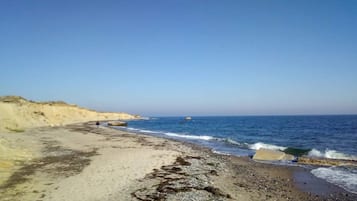 Una playa con cielo despejado, mar tranquilo y costa rocosa.