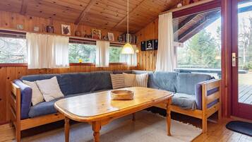 Interior acogedor de una cabaña con techo de madera, un sofá, una mesa y una ventana con cortinas.