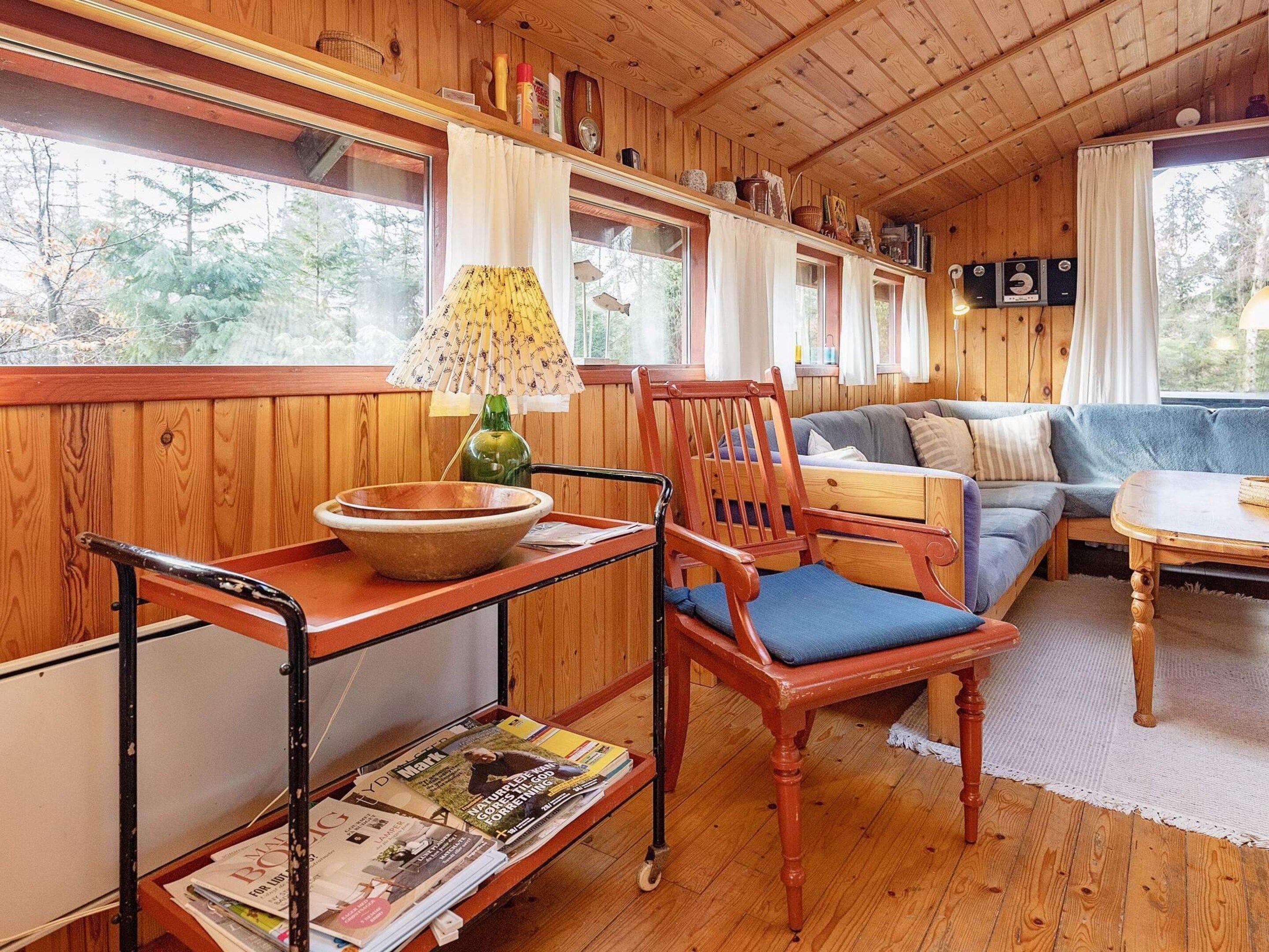 Interior acogedor de una cabaña con piso de madera, un sofá, una mesa de comedor y una ventana con cortinas.