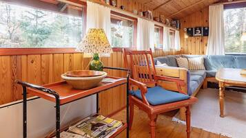 Interior acogedor de una cabaña con piso de madera, un sofá, una mesa de comedor y una ventana con cortinas.