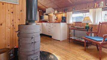 A rustic cabin interior with a wood stove, a dining area with a table and chairs, and a kitchen with cabinets and appliances.