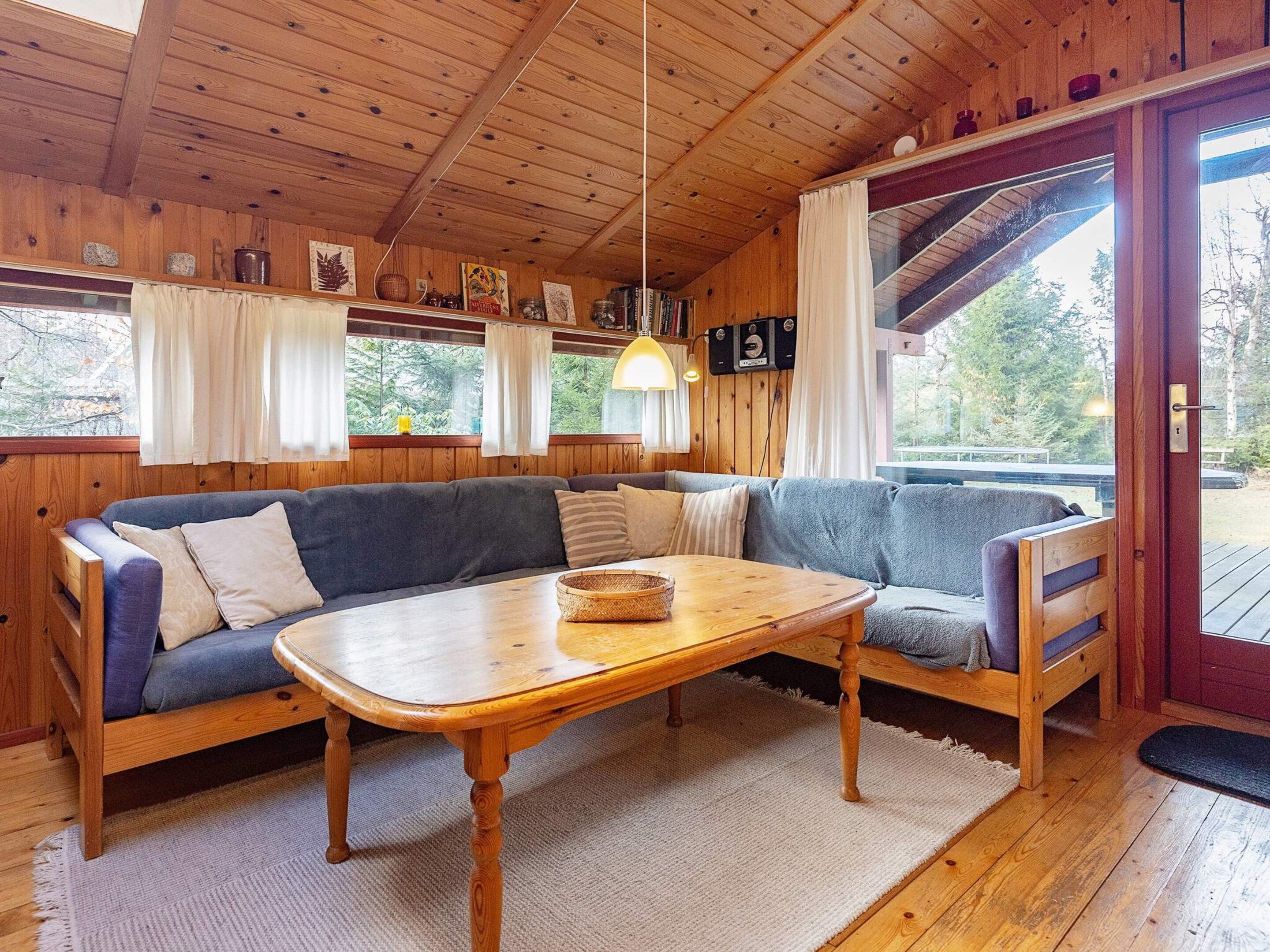 Interior acogedor de una cabaña con techo de madera, un sofá, una mesa y una ventana con cortinas.
