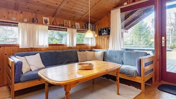 Interior acogedor de una cabaña con techo de madera, un sofá, una mesa y una ventana con cortinas.