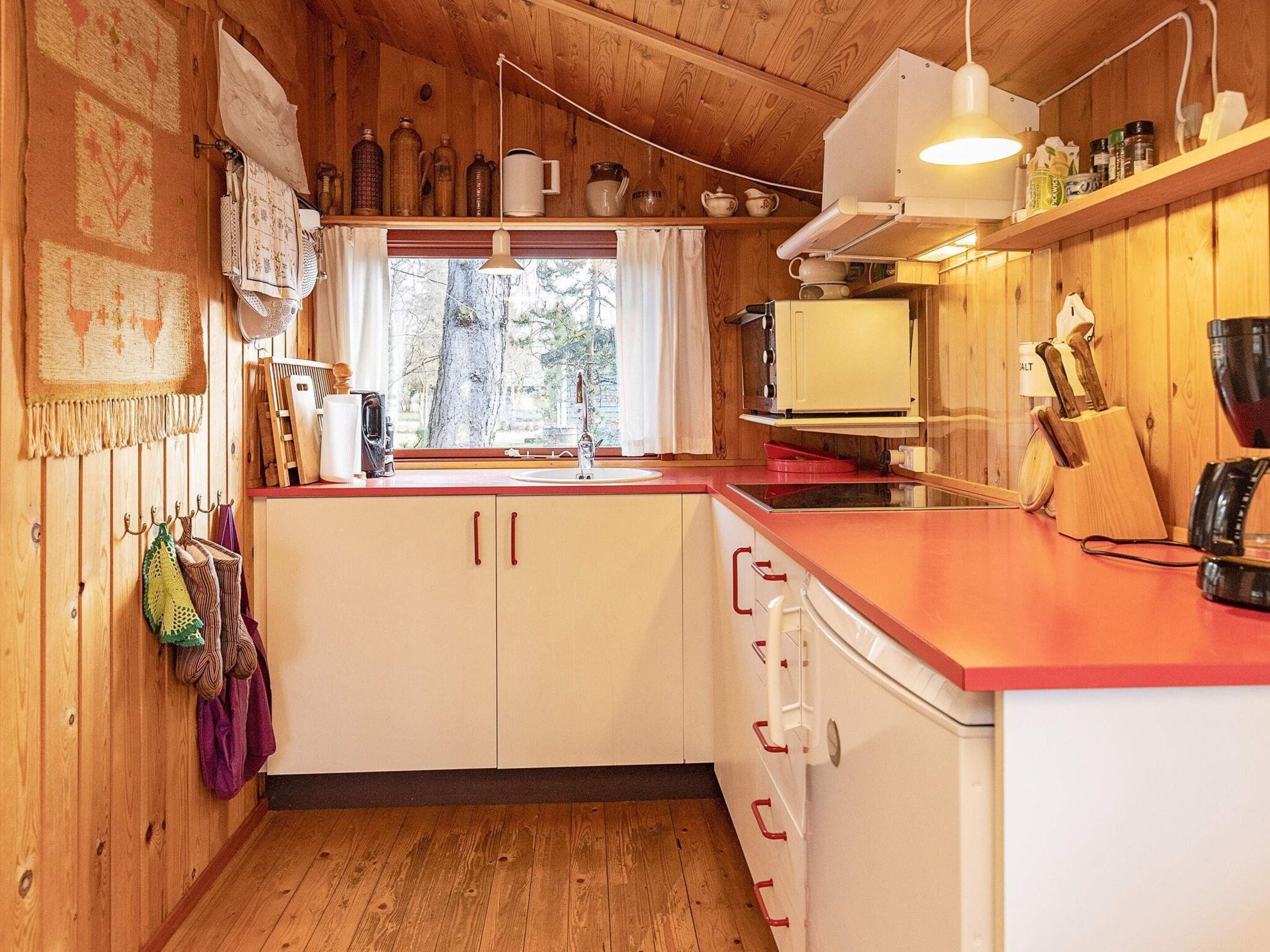 A kitchen with wooden cabinets, a red countertop, and a window with a view of trees.