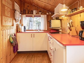 A kitchen with wooden cabinets, a red countertop, and a window with a view of trees. - 6 Person Holiday Home in Gedser (Gedser)